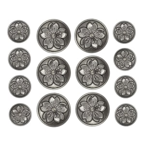 May include: A set of 12 silver-toned metal buttons with a floral design. The buttons are round and have a raised design of a flower with five petals.