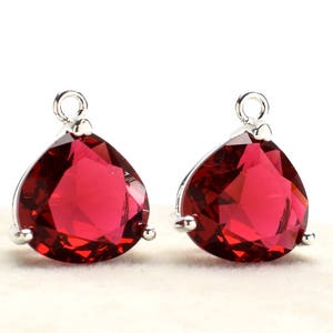 May include: Two teardrop-shaped, faceted, red gemstone pendants with silver-colored settings. Each pendant has a loop at the top for hanging. The gemstones are a deep, rich red color, and the settings are bright and shiny.