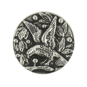 May include: Silver-toned metal button featuring a detailed design of a bird in flight with its wings spread wide. The bird is surrounded by stylized leaves and berries.