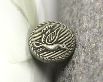 May include: Silver metal button with a detailed design of a bird in flight. The button has a textured, circular shape with a raised edge.