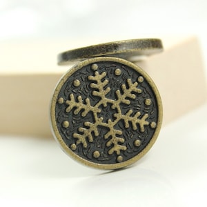 May include: A close-up of a gold snowflake button with a black background. The button is round and has a raised snowflake design.