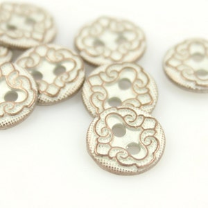 May include: A group of eight white buttons with a gold-coloured decorative design. The buttons have two holes.