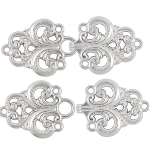 Op de afbeelding: Zilverkleurige metalen sluiting met een decoratief, versierd ontwerp. De sluiting bestaat uit twee delen, elk met een lus aan het ene uiteinde en een haak aan het andere uiteinde. De sluiting is perfect om kleding of knutselwerk een vleugje elegantie te geven.