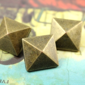 May include: Three antique gold pyramid-shaped studs. The studs have a square base and a pointed top. The studs are made of metal and have a distressed finish.