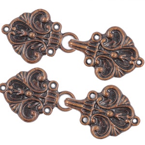 May include: Two ornate copper-colored metal clasps with a decorative floral design. Each clasp has a loop on one side and a hook on the other.