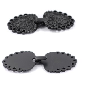 May include: Two black metal decorative clasps with a floral design. The clasps are connected by a metal loop.
