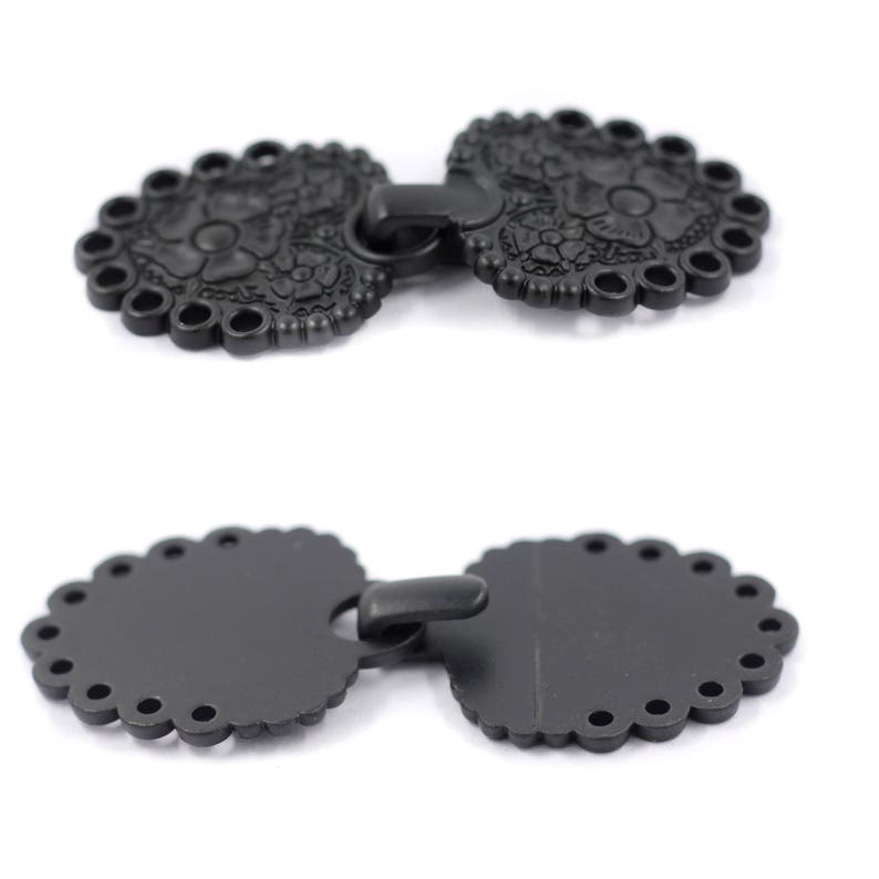 May include: Two black metal decorative clasps with a floral design. The clasps are connected by a metal loop.