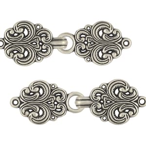Könnte beinhalten: Zwei silberfarbene Metallschließen mit filigranen Blumendesigns. Jede Schließe hat an einem Ende eine Schlaufe und am anderen Ende einen Haken.