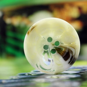 Könnte beinhalten: Ein weißer und brauner, marmorierter Glasknopf mit vier grünen Punkten in der Mitte.