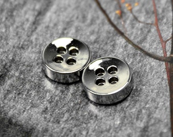 May include: Two silver metal buttons with four holes each. The buttons are round and have a shiny finish.