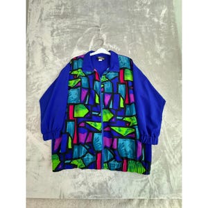 May include: A vintage blue jacket with a vibrant geometric pattern in shades of green, purple, and pink. The jacket features a full zipper, a collared neckline, and elastic cuffs. The sleeves and back are solid blue.