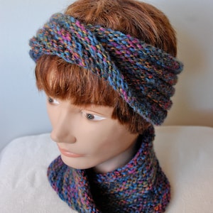 May include: A blue, black, and pink knit headband and matching neck warmer. The headband is twisted and tied at the top.