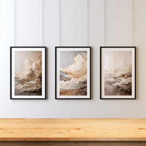 Könnte beinhalten: Drei gerahmte abstrakte Gemälde in Beige- und Brauntönen. Die Gemälde zeigen stilisierte Wolken in einer malerischen Art.