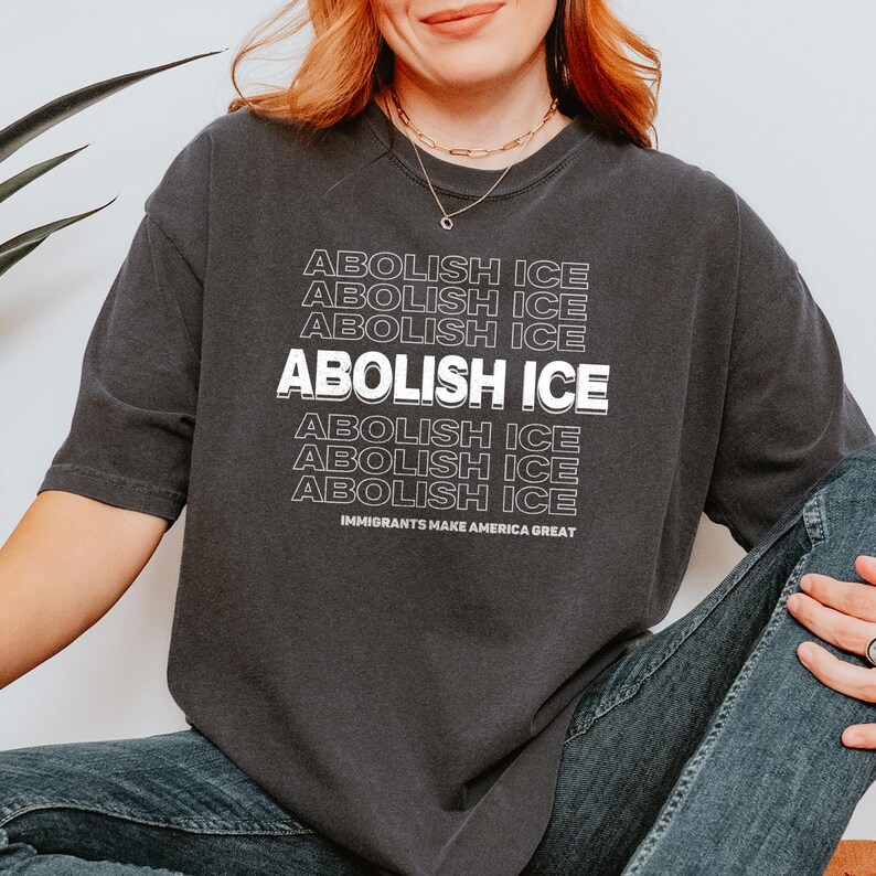 Puede incluir: Camiseta gris oscuro con la frase "ABOLISH ICE" en blanco apilado. La frase "IMMIGRANTS MAKE AMERICA GREAT" est&aacute; impresa debajo. La camiseta es de estilo casual.