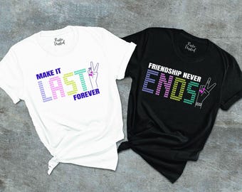 May include: Two white t-shirts with black text and graphics. The first shirt says "Make it Last Forever" with a peace sign. The second shirt says "Friendship Never Ends" with a peace sign.