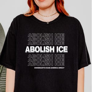 Puede incluir: Camiseta negra con la frase "ABOLISH ICE" en fuente blanca apilada. La frase "IMMIGRANTS MAKE AMERICA GREAT" est&aacute; impresa debajo. La camiseta es de estilo casual.