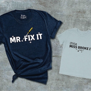May include: Two t-shirts, one navy blue and one light gray. The navy blue shirt has a white screwdriver and the text "MR. FIX IT". The light gray shirt has the text "little MISS BROKE IT" in black.