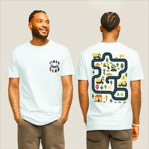 May include: White t-shirt with the text "Tired Dad's Club" on the front. The back of the shirt features a colorful road map design with construction vehicles, trees, and a house. The design includes a stop sign and caution symbols.