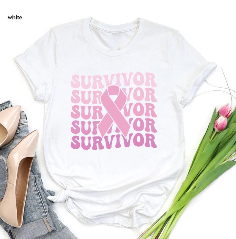 May include: White t-shirt with the word "SURVIVOR" in pink, stacked vertically with a pink ribbon graphic. The shirt is a crew neck style. The word "white" is in the top left corner of the image.