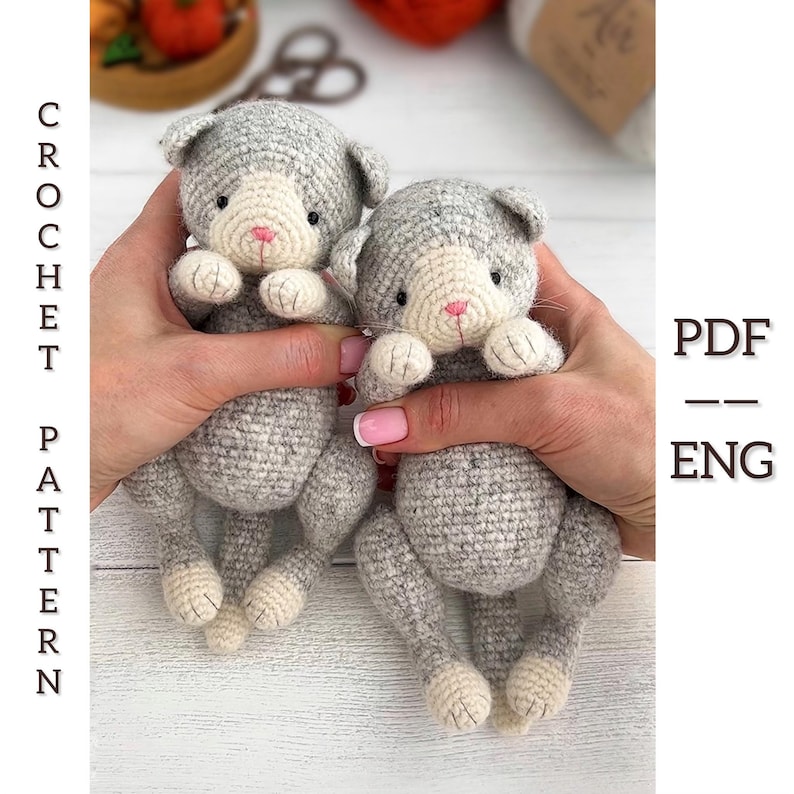 May include: Two gray and white crochet cat toys with pink noses and small black eyes are held up. The text "CROCHET PATTERN" is on the left side of the image, and "PDF - ENG" is on the right side.