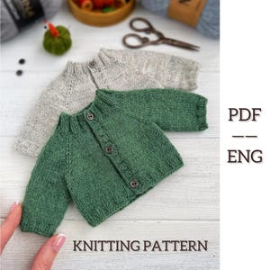 Puede incluir: Dos cárdigans de bebé tejidos, uno en verde apagado y otro en gris claro, se muestran sobre una superficie blanca. El cárdigan verde tiene botones oscuros. La imagen también incluye el texto "KNITTING PATTERN" y "PDF -- ENG".
