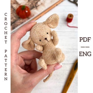 May include: A crocheted beige bunny toy with large ears and a small tail. The bunny is held in a hand. Text on the left side reads "CROCHET PATTERN". Text on the right side reads "PDF - ENG".