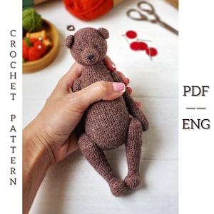May include: A handmade brown crochet teddy bear. The bear is held in a person's hands. The text "CROCHET PATTERN" is on the left side of the image, and "PDF - ENG" is on the right side.