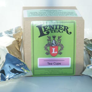 May include: A box of Lenier Tea Tea Cups. The box is brown with a green and white label. The label has the Lenier Tea logo, a crest with an L, and the words "Tea Cups".