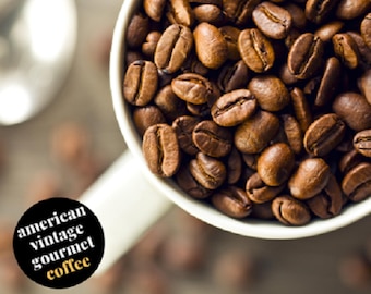 Könnte beinhalten: Nahaufnahme einer weißen Keramiktasse, gefüllt mit gerösteten Kaffeebohnen. Die Tasse hat ein schwarzes Etikett mit der Aufschrift "american vintage gourmet coffee".