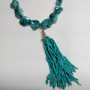 May include: A turquoise necklace with a tassel made of turquoise beads. The necklace is made of large, irregular shaped turquoise stones.