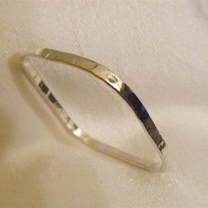 May include: A silver ring with a hammered texture. The ring has a geometric shape and a polished finish, reflecting light. The ring is a simple, elegant piece of jewelry.