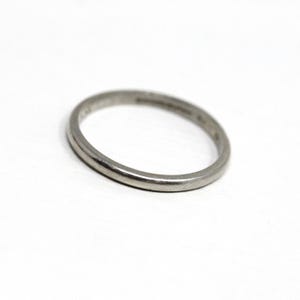 May include: A silver ring with a smooth, rounded band. The ring is set against a white background, highlighting its simple design. The ring's surface reflects light, showcasing its metallic sheen. A classic piece of jewelry.