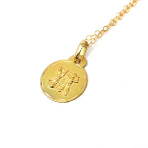 Peut inclure: Un collier avec un pendentif doré. Le pendentif rond présente un motif en relief de deux figures. Le pendentif est attaché à une fine chaîne dorée. Le charme a un bord texturé et une boucle pour la chaîne.