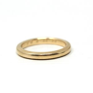 May include: A gold-colored ring with a smooth, rounded band. The ring is set against a white background, highlighting its simple design. The ring appears to be made of a solid metal, possibly gold or a gold alloy.