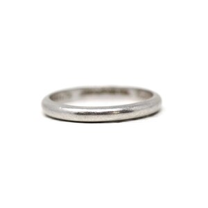 May include: A silver ring with a rounded band, set against a white background. The ring appears to be made of a solid metal, with a slightly worn or aged appearance. The ring is a simple, classic design.