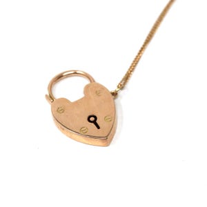 Può includere: Una collana con pendente a forma di lucchetto a forma di cuore color oro. Il pendente ha un buco della serratura ed è attaccato a una delicata catena. Il lucchetto è fissato con piccole viti.