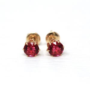 Puede incluir: Un par de pendientes de botón con piedras preciosas rojas vibrantes engastadas en oro. Los pendientes tienen un diseño clásico, con las piedras preciosas en un lugar destacado. El engaste de oro añade un toque de elegancia a la joyería.