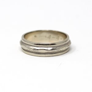 May include: A silver-colored ring with a textured design. The ring features a series of horizontal bands with a wavy pattern in the center. The ring is set against a white background.