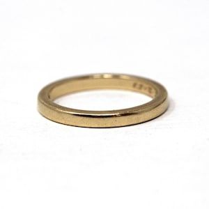 May include: A gold-colored ring with a smooth, rounded band. The ring is set against a white background, highlighting its simple design. The ring appears to be approximately 0.1 inches wide.