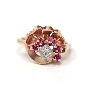 Peut inclure: Une bague en or rose avec un motif floral. La bague présente un groupe de petites pierres précieuses roses vives et un diamant central de forme carrée. La bague est posée sur un fond blanc.