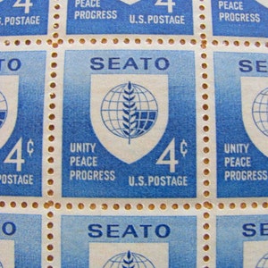 Puede incluir: Una hoja de cuatro sellos postales de Estados Unidos de 4 centavos con el logotipo de la OTASE. El logotipo es un escudo con un globo terráqueo y una espiga de trigo. El texto "SEATO" está impreso sobre el logotipo. El texto "Unity Peace Progress" está impreso debajo del logotipo. El texto "U.S. Postage" está impreso debajo del valor del sello.