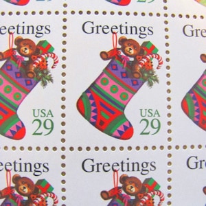May include: Four vintage Christmas postage stamps featuring a red and green stocking with a teddy bear inside. The stamps are labeled "Greetings" and "USA 29".