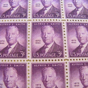 May include: Sheet of vintage U.S. postage stamps featuring a portrait of Alfred E. Smith. The stamps are a shade of purple with the text "U.S. POSTAGE 3¢" and "ALFRED E. SMITH" printed on them. The years 1873 and 1944 are also visible.