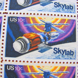 Peut inclure: Une planche de quatre timbres-poste américains de 10 cents représentant une illustration colorée de la station spatiale Skylab en orbite autour de la Terre. Les timbres sont bleus, rouges, jaunes et violets avec le texte "Skylab" et "US 10c" imprimé sur chaque timbre.
