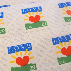 May include: A sheet of self-adhesive stamps with a red heart and sun design. The stamps say "LOVE" in blue letters and "USA" and "29" in black letters.