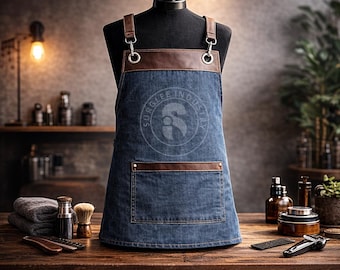 May include: A blue denim barber apron with brown leather accents, displayed on a mannequin. The apron has adjustable straps and multiple pockets. Text on the apron reads "BARBER APRON". The apron is durable, stylish, and comfortable.