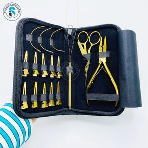 May include: A black zippered case containing gold-colored tools. The tools include scissors, pliers, clips, and curved metal pieces. The case is open, revealing the tools against a black interior. The brand name "SURGLEE INDUSTRY" is visible on the top left.