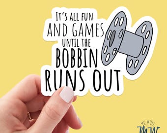May include: A sticker featuring the phrase "IT'S ALL FUN AND GAMES UNTIL THE BOBBIN RUNS OUT" and a grey sewing machine bobbin illustration. The background is yellow. The design includes the text "MC WOLL DESIGNS".