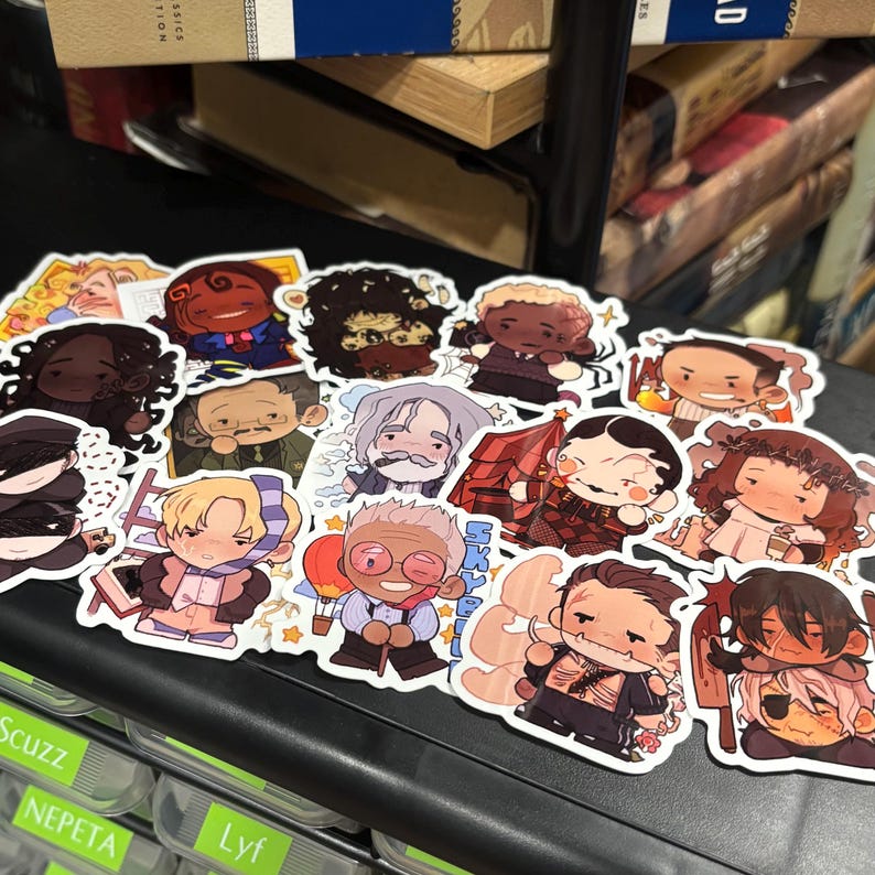 May include: A selection of vibrant character stickers, each showcasing distinct designs and expressions. The stickers depict various cartoon figures with detailed illustrations, including people with different hairstyles and outfits. The stickers are arranged on a black surface.