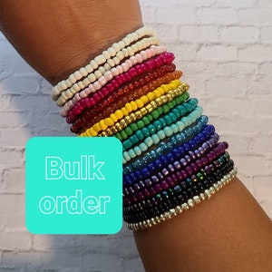Puede incluir: Una pila de pulseras de cuentas de colores en un patrón de arcoíris. Las pulseras están apiladas en la muñeca de una persona. El texto "Bulk order" está en la esquina inferior izquierda de la imagen.